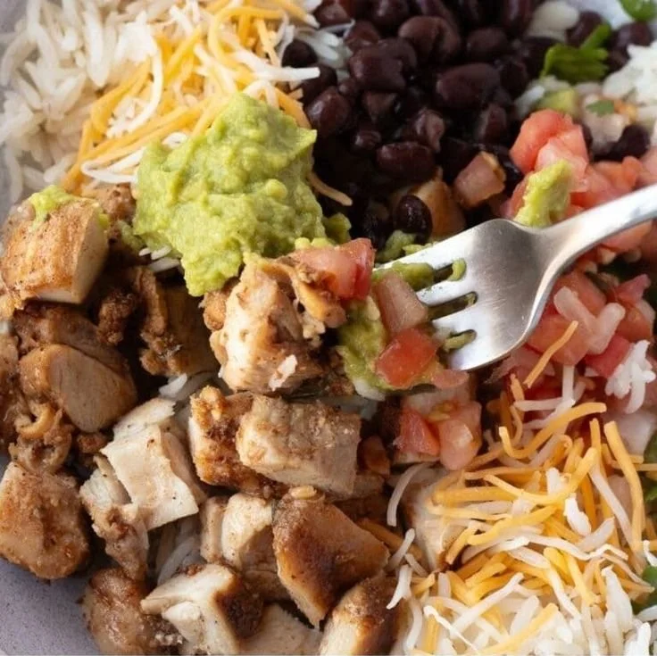 Grilled chicken burrito bowl with rice and beans garnished with fresh ingredients
